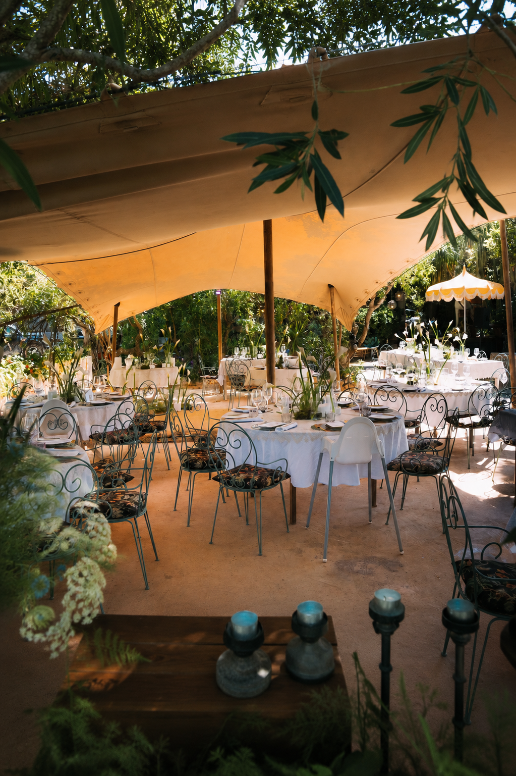 Outdoor hospitality setting surrounded by nature, featuring elegantly dressed tables, floral installations and bespoke styling under a canopy for a private celebration.